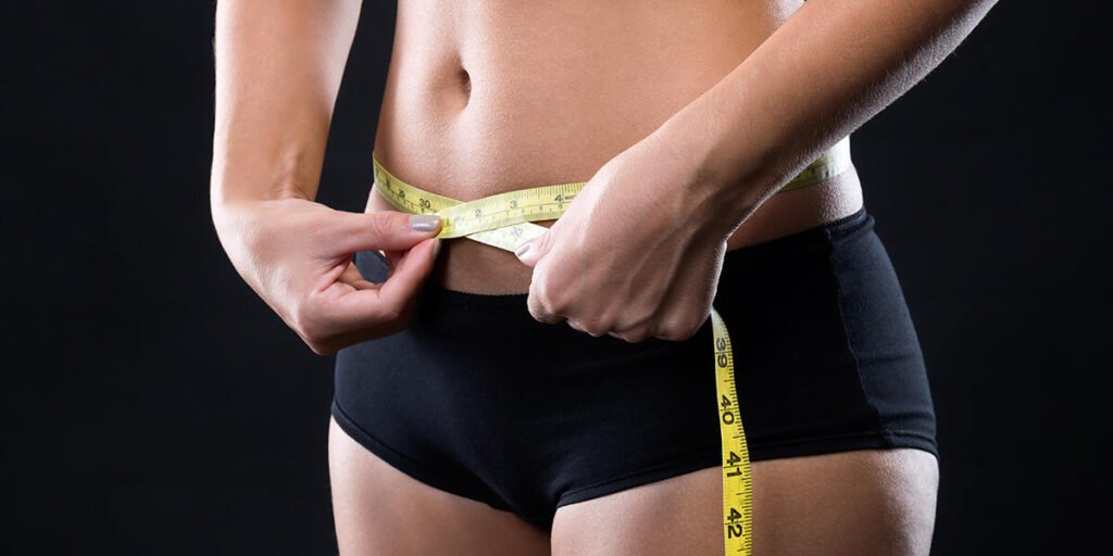 A woman measures her waist with a tape measure to track progress during awake liposuction recovery.